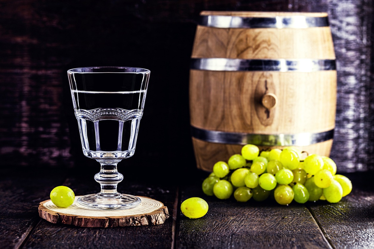 Glass of Grappa on wooden background with old oak barrel
