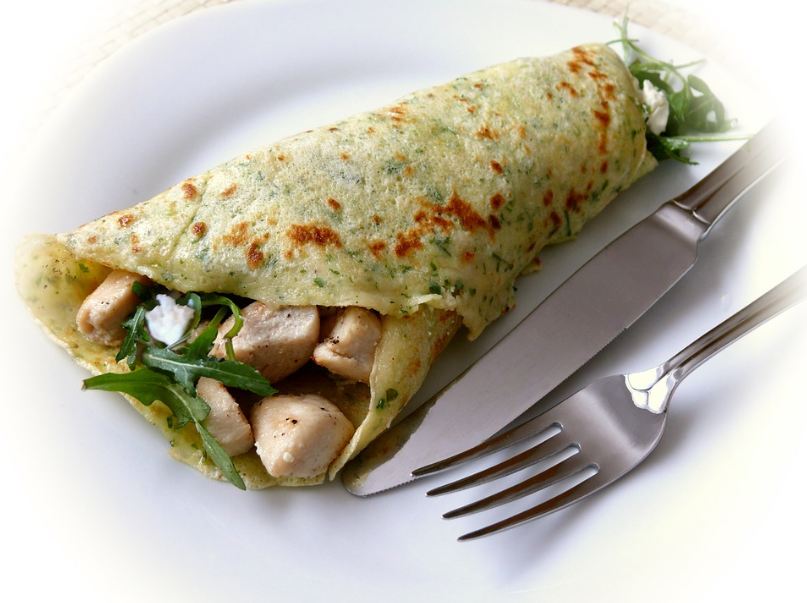 a crepe with a savory filling on a plate, knife, fork