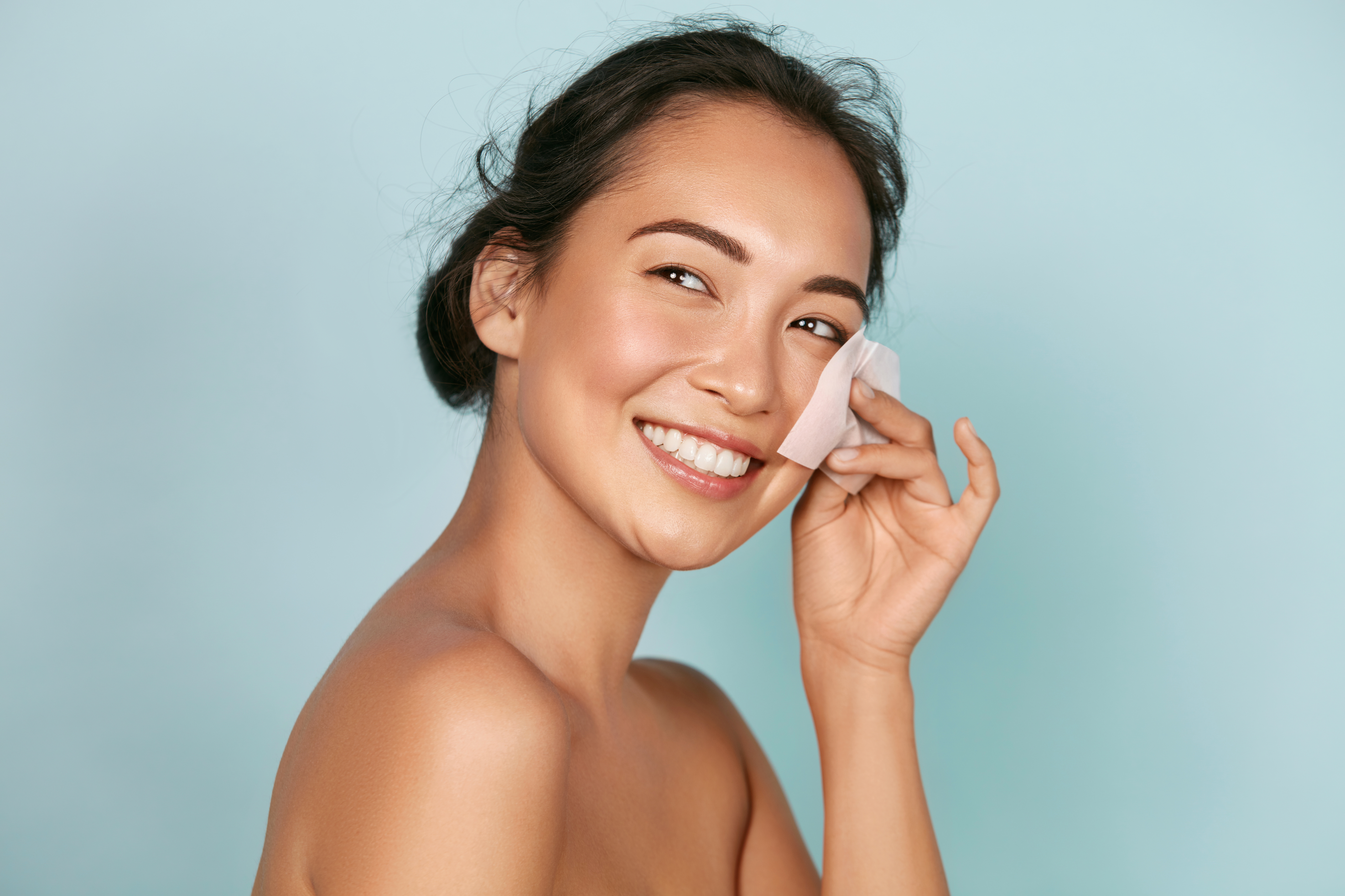 Face skin care. Smiling woman using facial oil blotting paper po