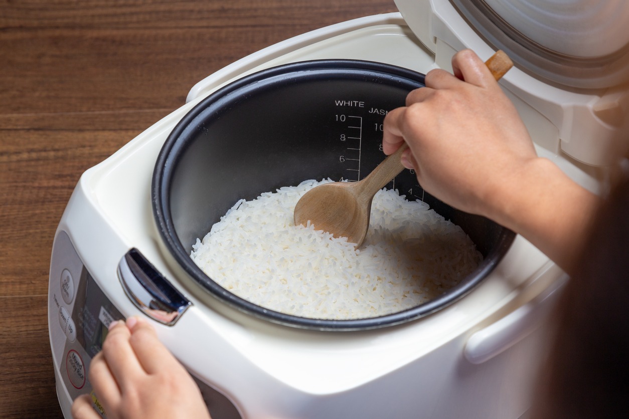 Woman's hand is scooping jasmine rice cooking in the electric rice cooker