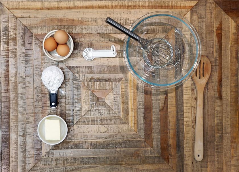 measuring cup with flour, measuring spoons, bowl, empty bowl with whisk, ladle, bowl with egg, bowl with butter