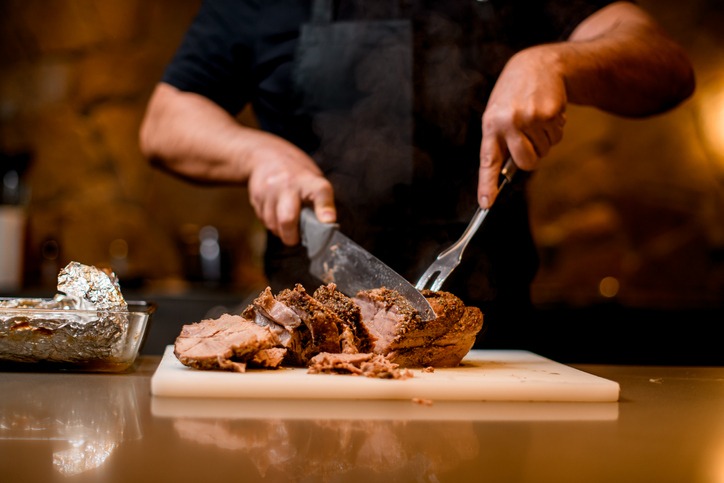view on fried meat which man cuts to slices on cutting board.