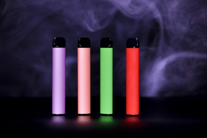 Set of colorful disposable electronic cigarettes on a black background with colour smoke. The concept of modern smoking, vaping and nicotine.