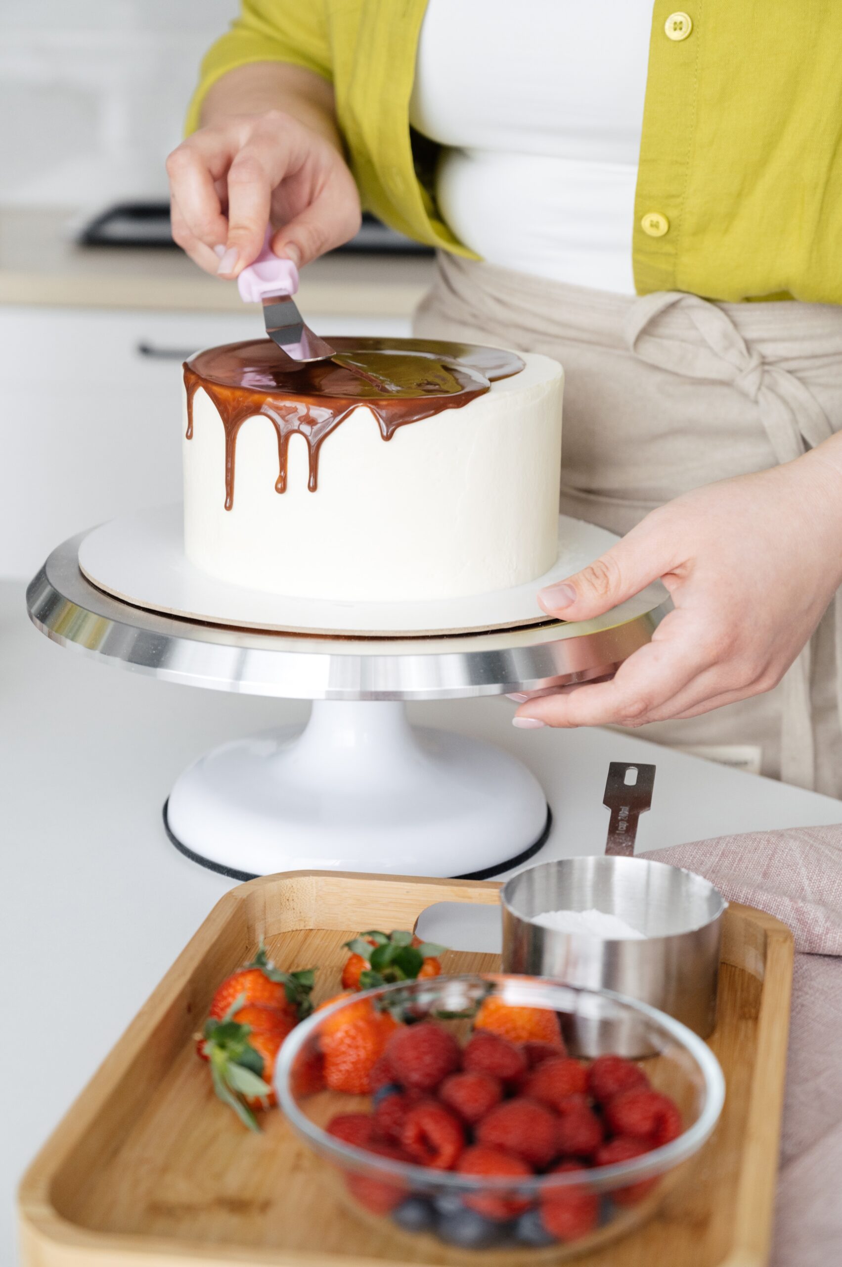 crop woman decorating cake with chocolate glaze on stand